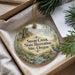 A decorative ornament with a scenic landscape, featuring a bird, is displayed in a box with pine branches.