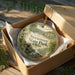 A decorative ornament in a brown box, featuring a scenic landscape with a bridge and trees, with the text "Sycamore State Park, Ohio" printed on it.