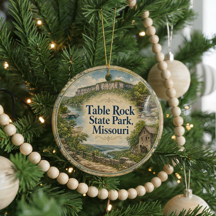 A round ornament hanging on a Christmas tree, featuring a scenic landscape with a waterfall and a house.