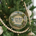 A round ornament hanging on a Christmas tree, featuring a scenic landscape with a waterfall and a house.