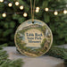 A round ornament with a scenic landscape of Table Rock State Park, Missouri, featuring a waterfall and a cabin, is displayed on a table with pine branches in the background.