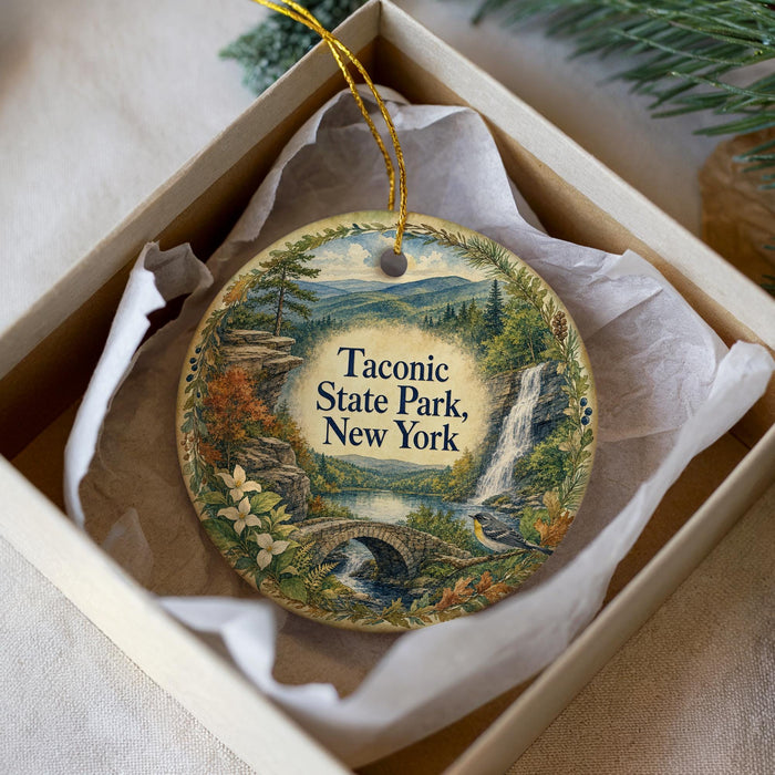 A decorative ornament in a box, featuring a scenic landscape with a waterfall, bridge, and trees.