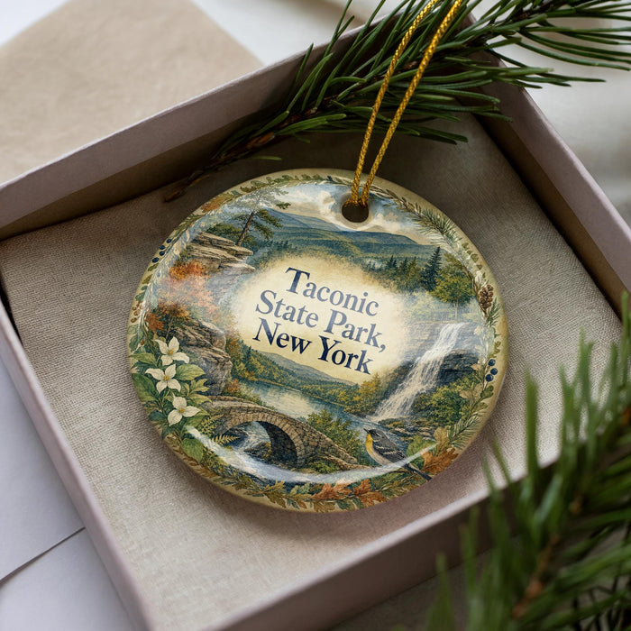 A decorative ornament in a box, featuring a scenic landscape with a waterfall and pine trees.