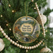 A round ornament hanging on a Christmas tree, featuring a scenic landscape with a waterfall and a bridge.