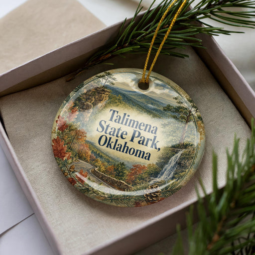 A decorative ornament in a box, featuring a scenic landscape with mountains, trees, and a waterfall.
