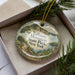 A decorative ornament in a box, featuring a scenic landscape of the Tallman Mountain in New York.