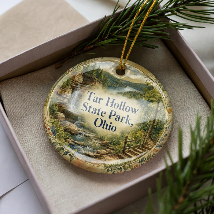 A decorative ornament with a scenic landscape of a waterfall and forest, placed in a box with pine branches.
