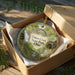 A decorative ornament in a box, featuring a scenic image of Tinkers Creek State Park in Ohio.