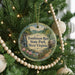 A round ornament hanging on a Christmas tree, featuring a scenic landscape with a waterfall and a path leading to a cabin.