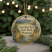A round ornament with a scenic mountain landscape and a cabin, hanging from a string.