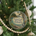 A round ornament hanging on a Christmas tree, featuring a scenic landscape of a lake and trees.