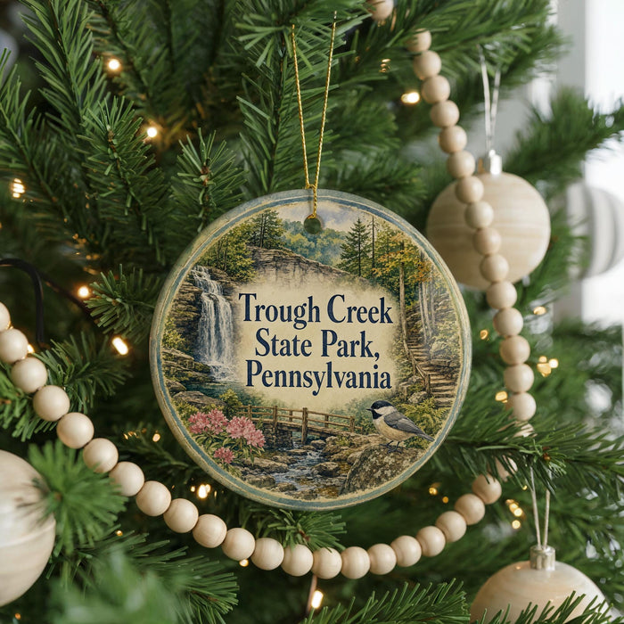 A round ornament hanging on a Christmas tree, featuring a scenic image of a waterfall and a bird.