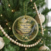 A circular ornament hanging on a Christmas tree, featuring a scenic image of a forest and a waterfall.