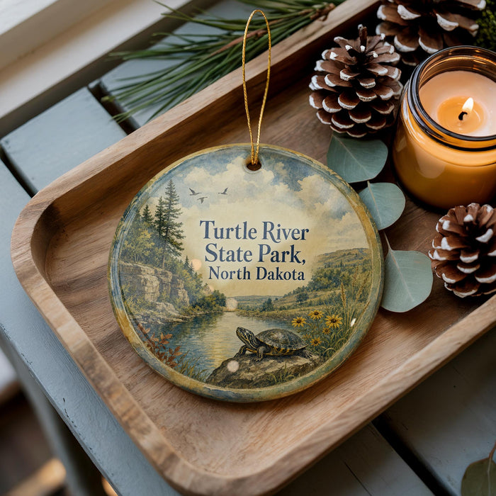 A decorative ornament featuring a turtle resting on a rock, surrounded by pine cones and a candle, placed on a wooden surface.