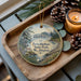A decorative ornament featuring a scenic landscape of Twin Harbors State Park in Washington, with pine cones and a lit candle on a wooden tray.