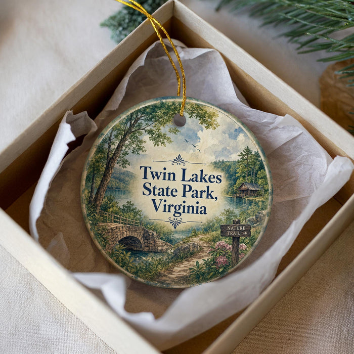 A decorative ornament in a white box, featuring a scenic landscape with a bridge, trees, and a lake.