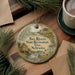 A decorative ornament featuring a scenic image of the Two Rivers State Recreation Area in Nebraska, with a waterfall and a house, is displayed on a wooden surface alongside a cup of coffee and some pine branches.