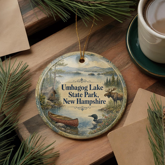 A decorative ornament featuring a moose, canoe, and pine tree, with the text "Umbagog Lake State Park, New Hampshire" displayed on it.