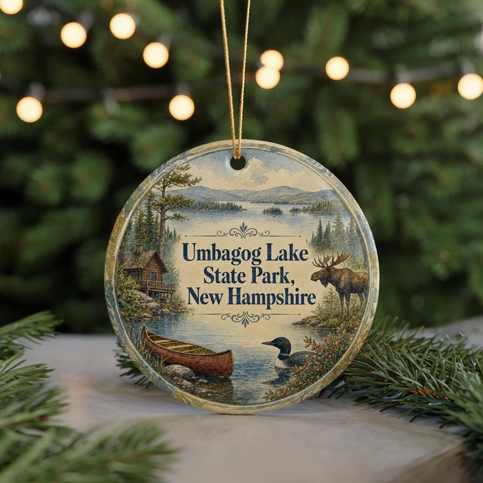 A round ornament featuring a moose, canoe, and loon in a scenic landscape, with the text "Umbagog Lake State Park, New Hampshire" displayed prominently.