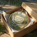 A round ornament in a box, featuring a scenic landscape with a waterfall and a bridge, with the text "Underhill State Park, Vermont" displayed on it.