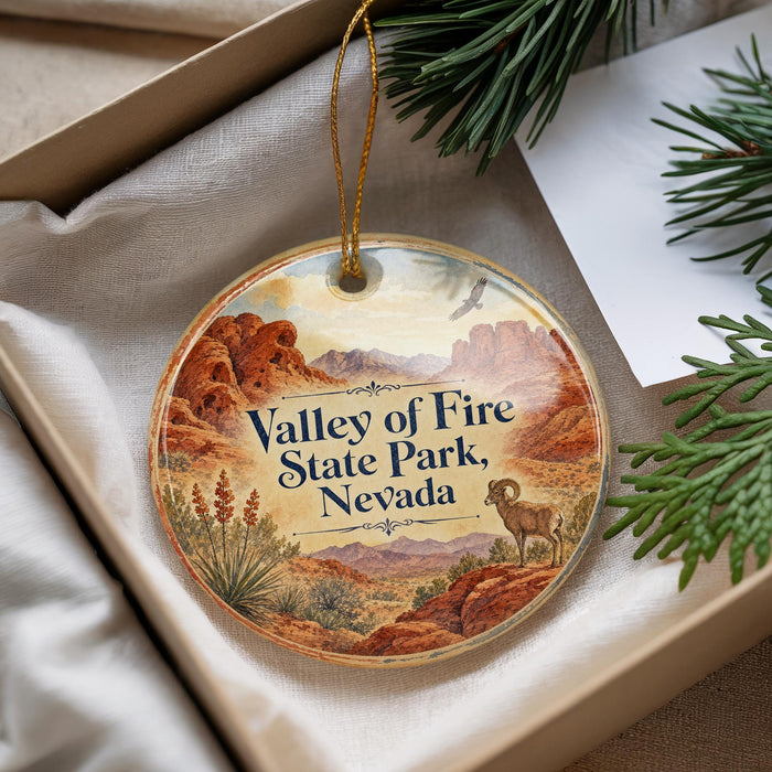 A decorative ornament with a landscape of mountains, desert, and a bighorn sheep, placed in a box with pine branches.