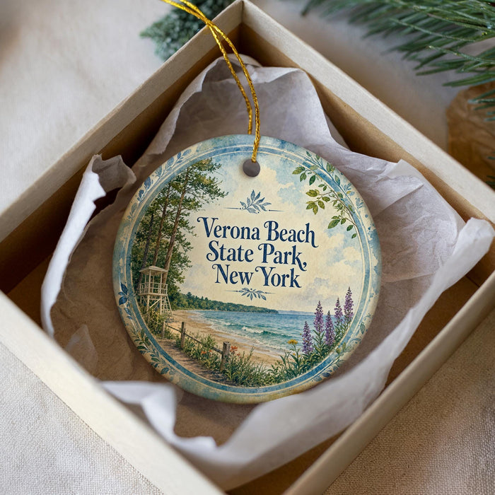 A round ornament with a scenic beach landscape and text, placed in a box with a white tissue paper lining.