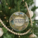 A round ornament hanging on a Christmas tree, featuring a scenic landscape with a house and a waterfall.