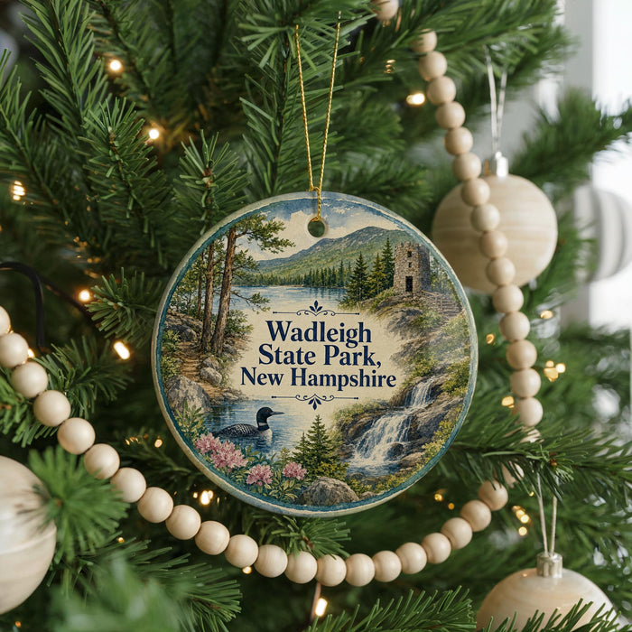 A round ornament hanging on a Christmas tree, featuring a scenic landscape with a waterfall and a bird in the foreground.