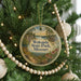 A circular ornament hanging on a Christmas tree, featuring a scenic landscape with a path leading to a cabin.