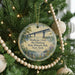 A round ornament hanging on a Christmas tree, featuring a scenic image of a bridge and greenery.