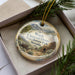 A decorative ornament in a box, featuring a scenic landscape with mountains and a chimney, with the text "Ward Charcoal Ovens State Historic Park, Nevada" printed on it.