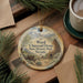 A decorative ornament featuring a scenic landscape with mountains, a lodge, and pine trees, hanging on a wooden surface.