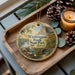 A decorative ornament featuring a scenic landscape of Washington Rock State Park, New Jersey, with pine cones and a lit candle on a wooden tray.