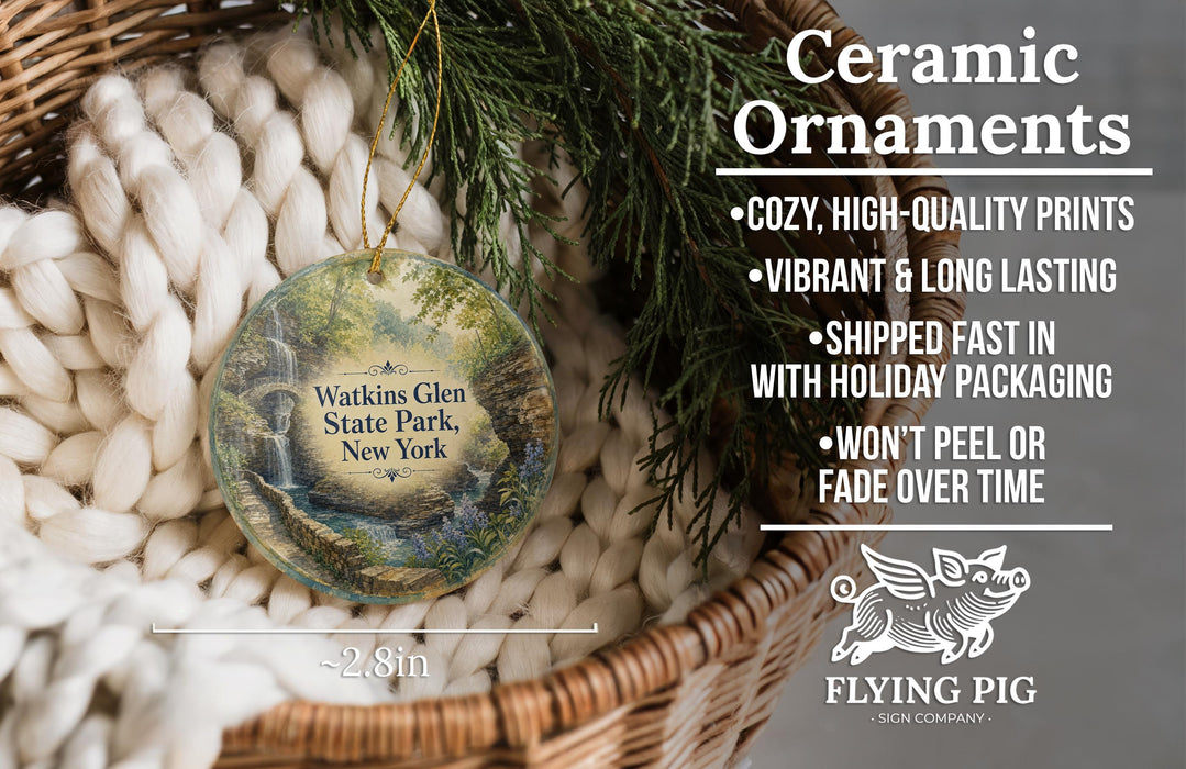 Ceramic ornaments, specifically a Warkins Glen State Park, New York ornament, are displayed in a basket with pine branches. The ornament features a scenic landscape with a waterfall and is described as cozy, high-quality prints, vibrant, and long-lasting. It is shipped fast in holiday packaging and does not peel or fade over time. The image also includes a scale indicating the ornament's size, with the text "2.8in" and a logo for "Flying Pig - SIGN COMPANY".