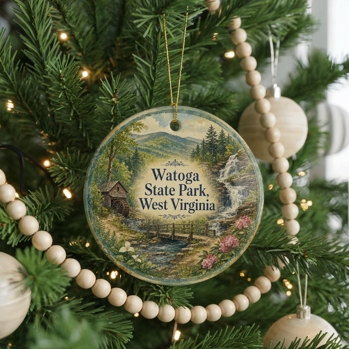 A round ornament hanging on a Christmas tree, featuring a scenic landscape with a waterfall and a cabin.