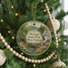 A round ornament hanging on a Christmas tree, featuring a scenic landscape with a waterfall and a cabin.