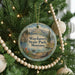 A round ornament hanging on a Christmas tree, featuring a scenic landscape with mountains, trees, and a lake.