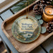 A wooden tray with a decorative ornament featuring a scenic landscape of Wellington State Park, New Hampshire, and pine cones.
