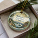 A circular ornament with a scenic landscape of Wellington State Park, New Hampshire, displayed in a box with pine branches.