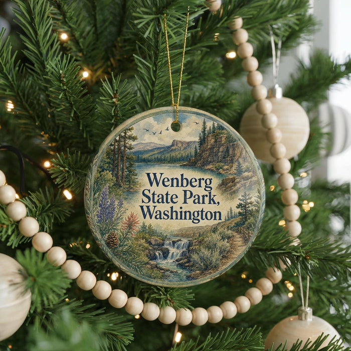 A round ornament hanging on a Christmas tree, featuring a scenic landscape with a waterfall and mountains.