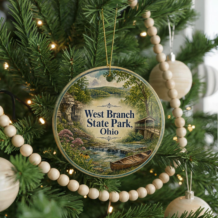 A round ornament hanging on a Christmas tree, featuring a scenic landscape with a river, bridge, and trees.