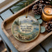 A decorative ornament featuring a scenic landscape of West Shore State Park, Montana, with a candle and pine cones on a wooden tray.