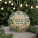 A round ornament with a painting of a beach scene, featuring a house, trees, and a body of water, hanging from a string.