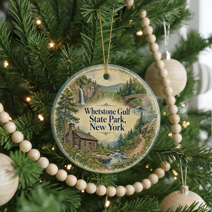 A round ornament hanging on a Christmas tree, featuring a scenic landscape with a cabin, trees, and a waterfall.
