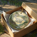 A decorative ornament in a wooden box, featuring a scenic landscape with a cabin and a waterfall.
