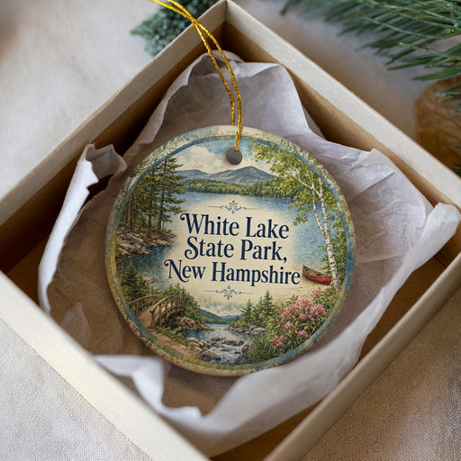 A decorative ornament in a box, featuring a scenic landscape with a lake, mountains, and a bridge.