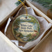 A decorative ornament in a box, featuring a scenic landscape with a lake, mountains, and a bridge.