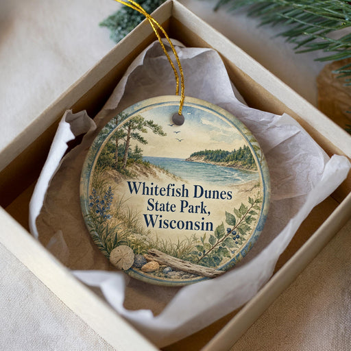 A round ornament in a box, featuring a scenic landscape with a lake, trees, and mountains, along with the text "Whitefish Dunes State Park, Wisconsin".