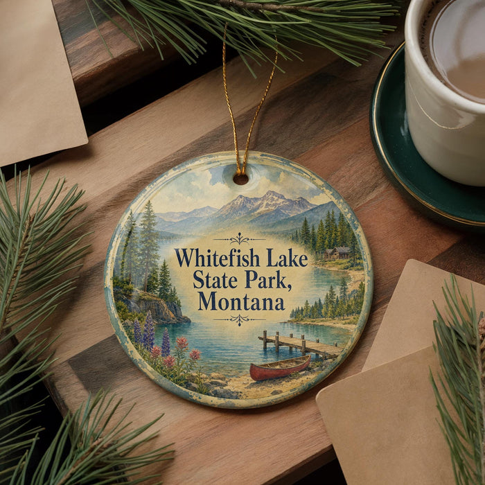 A decorative ornament featuring a scenic landscape of Whitefish Lake State Park, Montana, with a canoe on the lake and pine trees in the background.