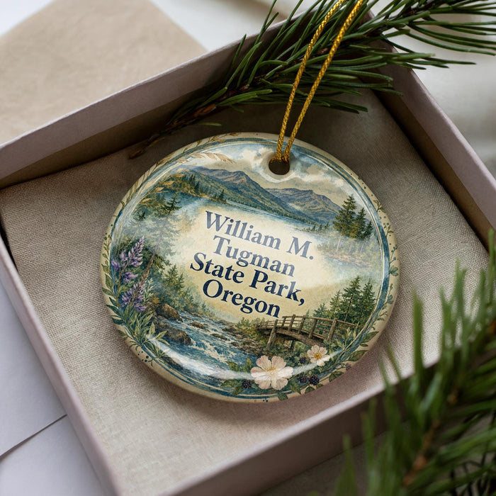 A decorative ornament in a box, featuring a scenic landscape with mountains, pine trees, and a river.